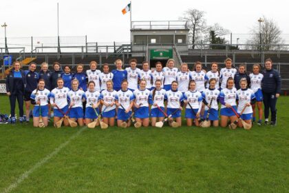 A women's team poses together on an outdoor field.