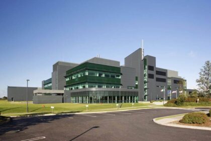 A modern office and industrial building with large glass windows, surrounded by a well-maintained lawn and an empty parking lot.