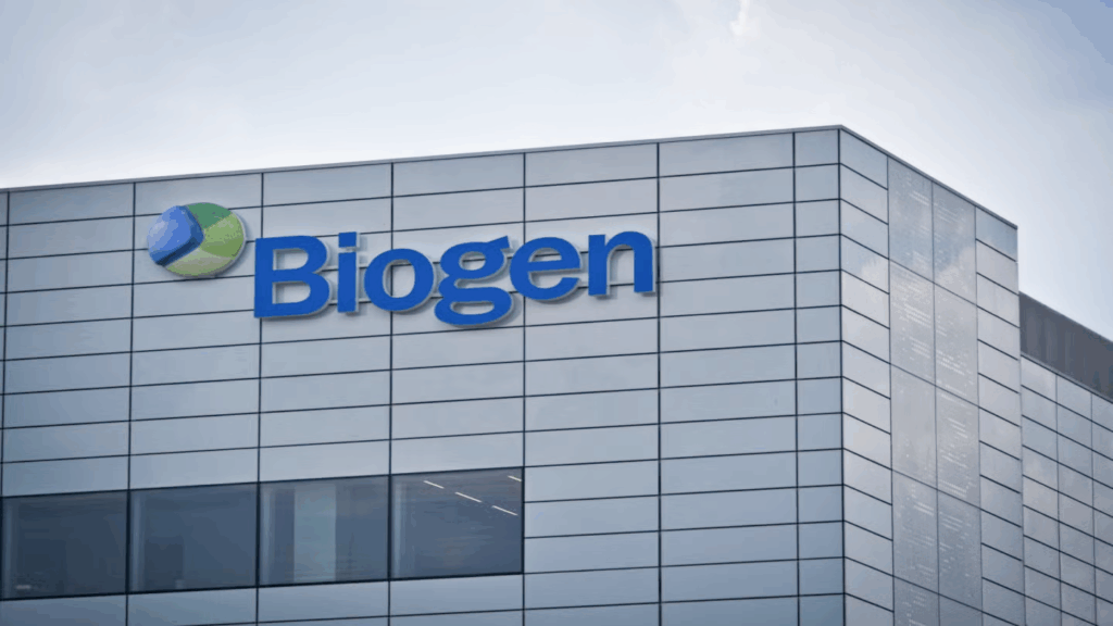 Close-up of the Biogen building exterior, showing the company’s blue and green logo and large blue “Biogen” text on a modern, reflective glass-panelled facade under a clear sky.