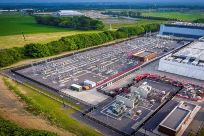 An aerial view of an electrical substation surrounded by green fields and buildings.