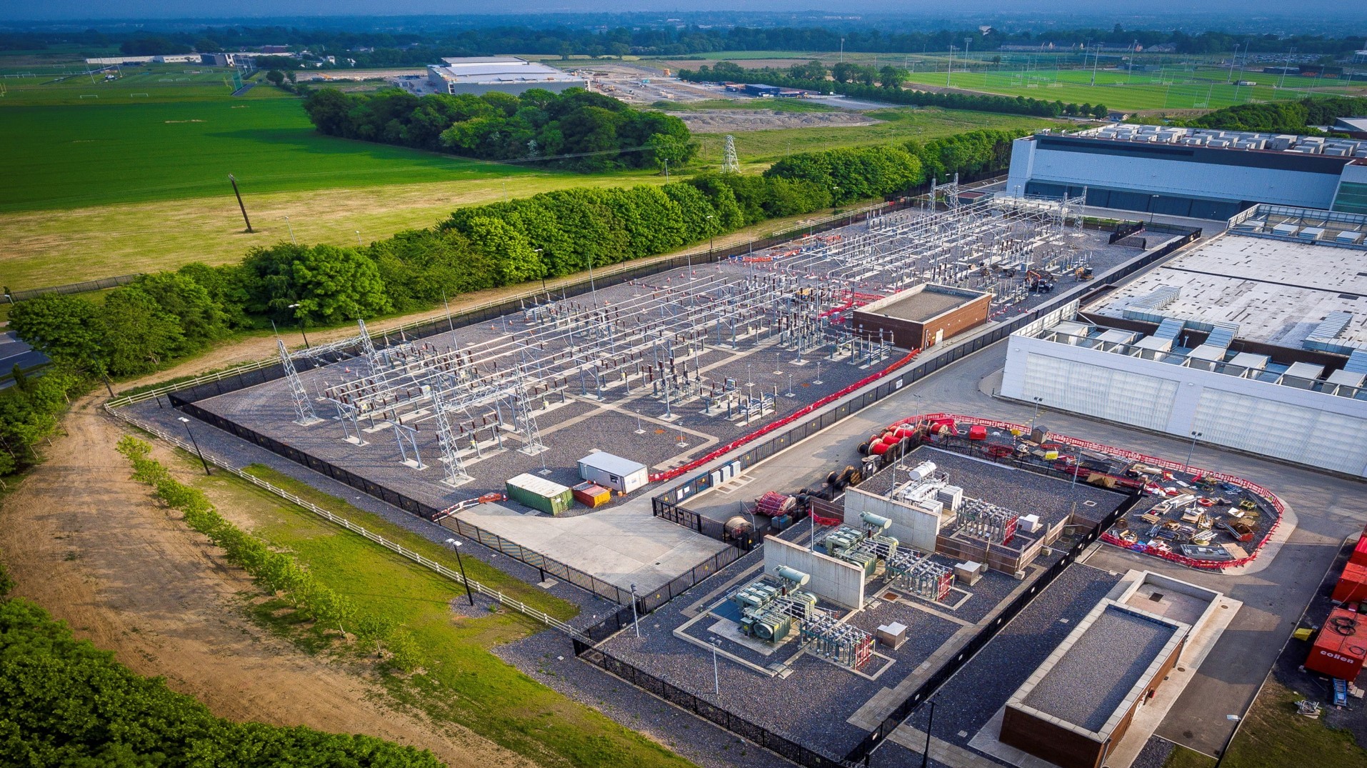 An aerial view of an electrical substation surrounded by green fields and buildings.