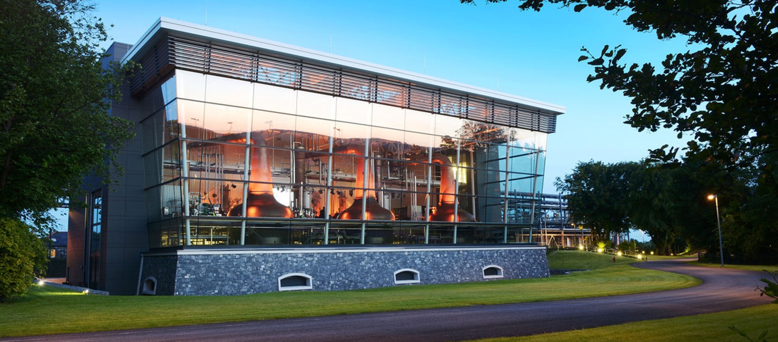 A modern building with large glass windows showcasing copper distillation tanks inside.