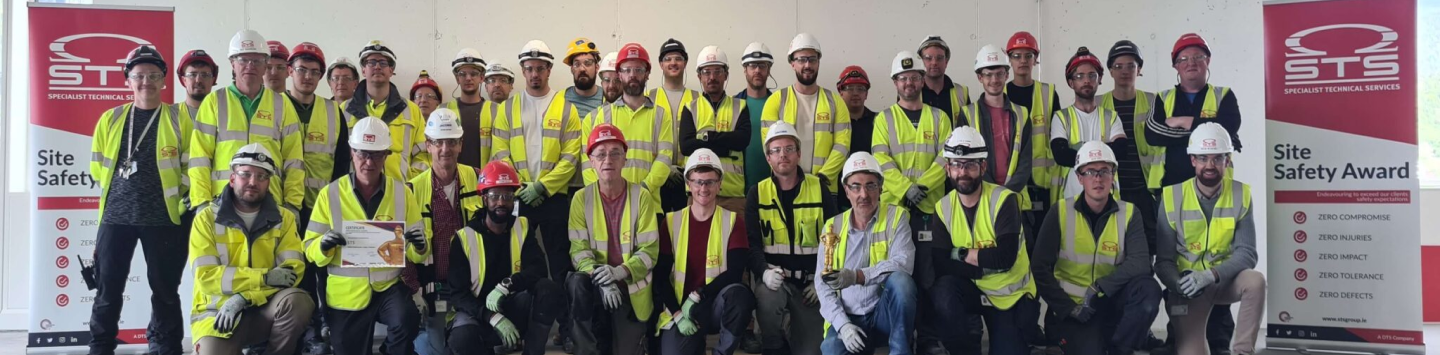 A group of construction workers in safety gear pose with a "Site Safety Award" banner.