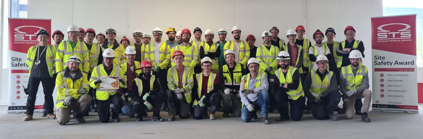 A group of construction workers in safety gear pose with a "Site Safety Award" banner.