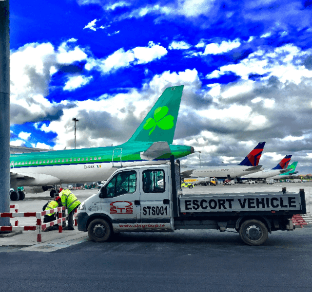 An escort vehicle parked next to an airplane on an airport tarmac.