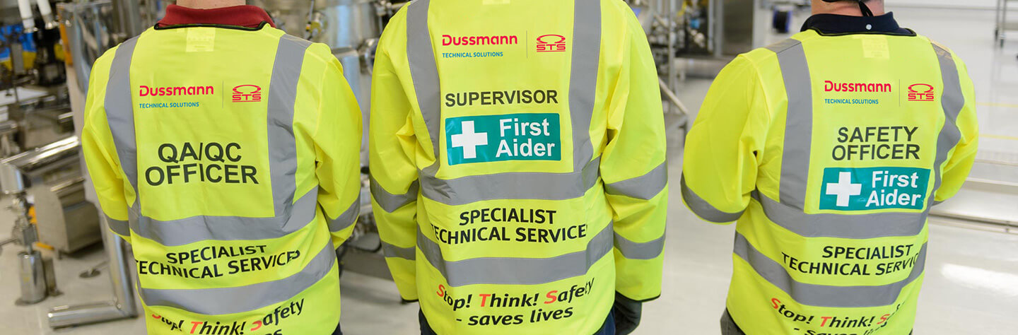 Three workers in high-visibility jackets labeled "QA/QC Officer," "Supervisor," and "Safety Officer" stand side by side.