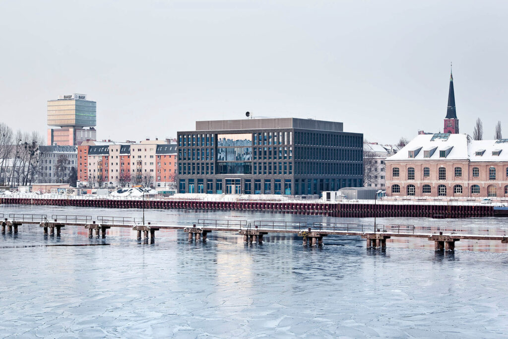 A snowy riverside view of Berlin with modern and historic buildings.