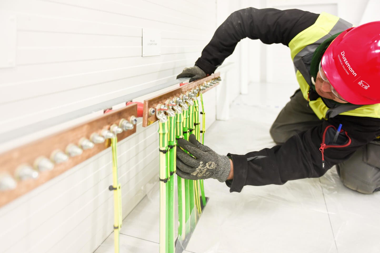 A worker in a hard hat and safety vest adjusts electrical connections.