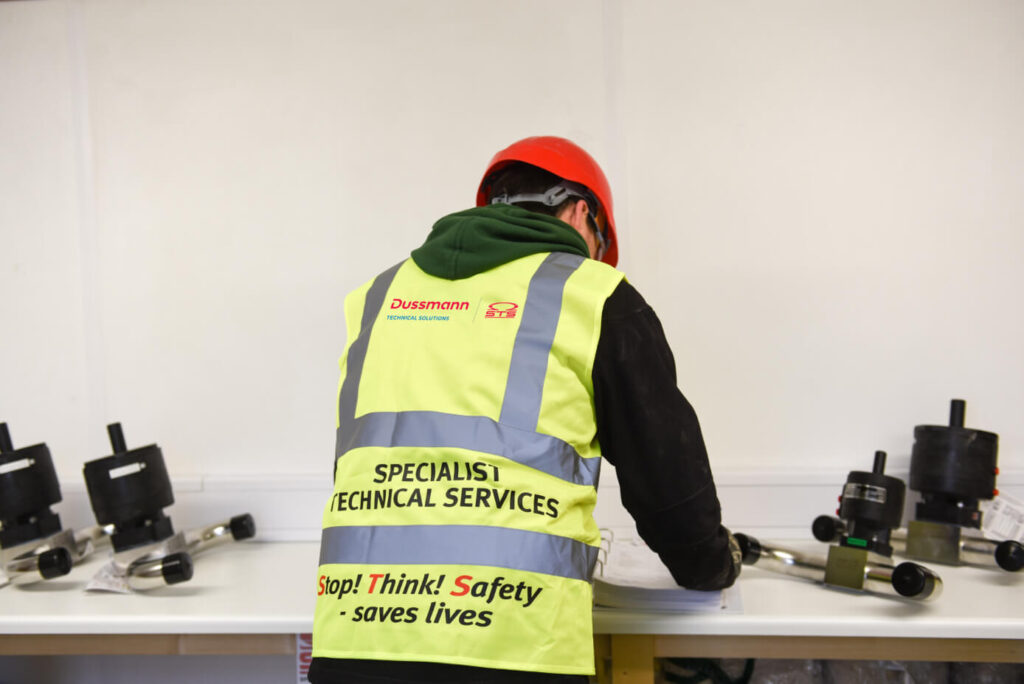 A worker in a high-visibility vest and red hard hat reviews documents at a table.