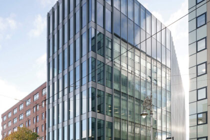 A modern glass office building on a street corner under a partly cloudy sky.