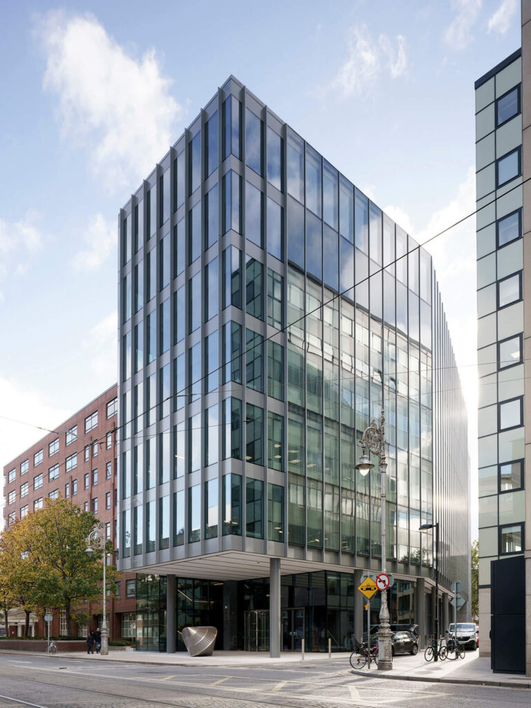 A modern glass office building on a street corner under a partly cloudy sky.