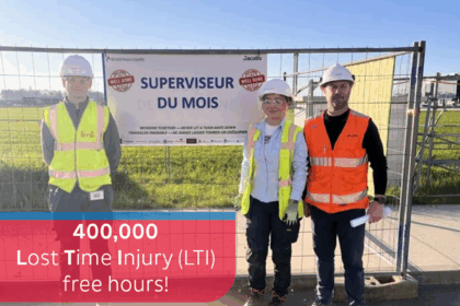 Three construction workers stand in front of a “Supervisor of the Month” sign at a worksite. They wear safety gear and high-vis vests. A banner reads “400,000 Lost Time Injury (LTI) free hours!” with Dussmann Technical Solutions and STS logos above.