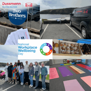A collage of photos celebrating National Workplace Wellbeing Day organized by Dussmann Technical Solutions and STS Group. The collage includes a group of smiling people posing by the ocean, yoga mats arranged indoors for a wellness activity, a box of assorted pastries, a branded Dussmann van parked by a coastal scene, pamphlets or flyers labeled “Team,” and a sign for “Two Brothers Coffee Company.” The center of the collage features the National Workplace Wellbeing Day logo with colorful icons representing health, fitness, and communication.